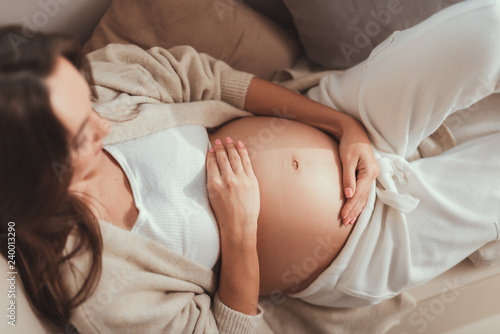 Careless lady lying and holding her hands on pregnant belly