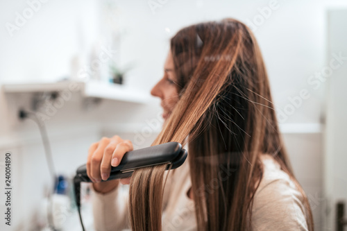 Young woman straightening her hair in the bathroom.