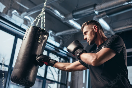 low angle view of handsome boxer training with punching bag in gym