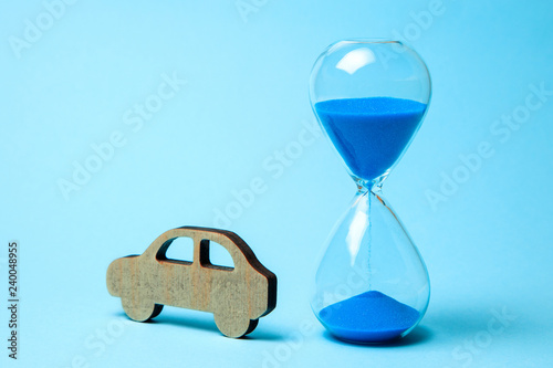 Depreciation or depreciation of the car over time. Wooden car and hourglass on blue background. Old car, second hand repair.