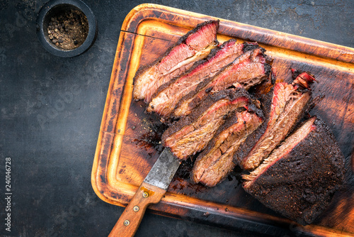 Traditional smoked barbecue wagyu beef brisket as piece and sliced offered as top view on an old cutting board with copy space left