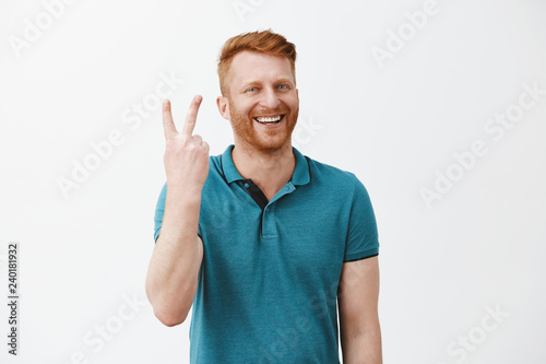 Showing you two steps to successful business. Portrait of friendly-looking happy and joyful redhead male with beard making sign twice and smiling broadly while standing over gray background