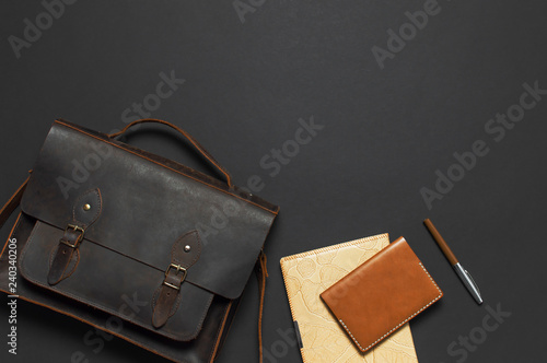 Fashionable concept. Brown leather men's bag, diary notebook, leather passport cover and pen on black background top view flat lay with copy space. Accessories businessman, stylish men's clothes