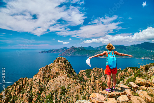 Happy tourist girl standing on the rock over the sea in Calanques de Piana Corsica on sunny summer day