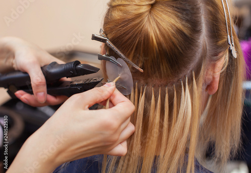 The hairdresser does hair extensions to a young girl, a blonde in a beauty salon. Professional hair care.