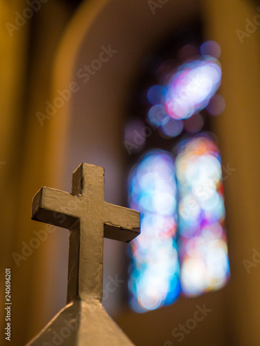 Cross inside church in foreground with blurry stained glass behind.