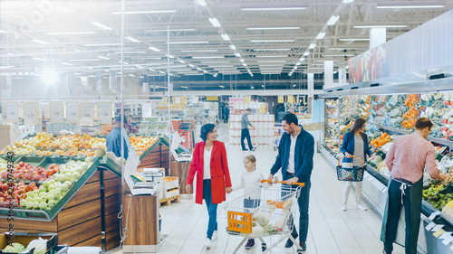 At the Supermarket: Happy Family of Three, Holding Hands, Walks Through Fresh Produce Section of the Store. Father, Mother and Daughter Having Fun Time Shopping. High Angle Panoramic Shot.