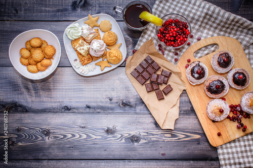 Happy New Year cranberries, sweets in a dessert plate, a broken chocolate bar on kraft paper and a glass of tea with lemon on a linen napkin on a dark gray background.
