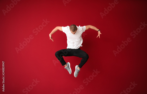 Young male dancer jumping against color background