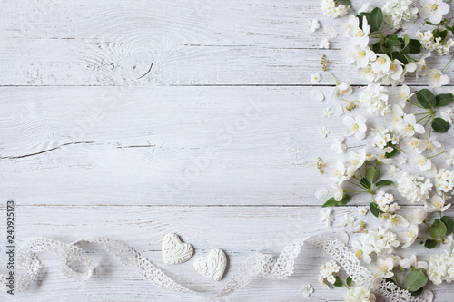 White wooden background with white spring flowers, hearts and lace ribbon