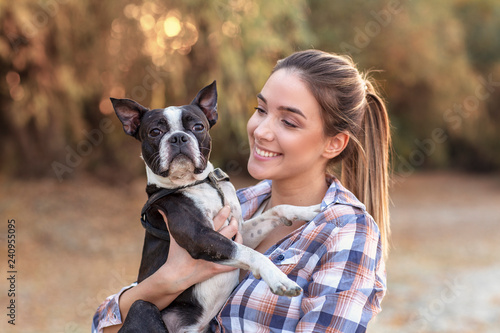 Young girl holding on hands her boston terrier black and white dog on the beach