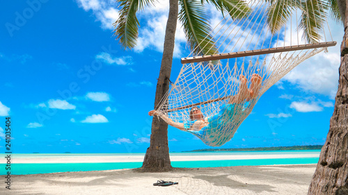 LOW ANGLE: Cheerful young woman relaxing under the palms in the comfy hammock.