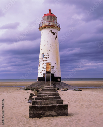 An old white lighthouse with a red roof on a sandy beach with the sea and sky in the background