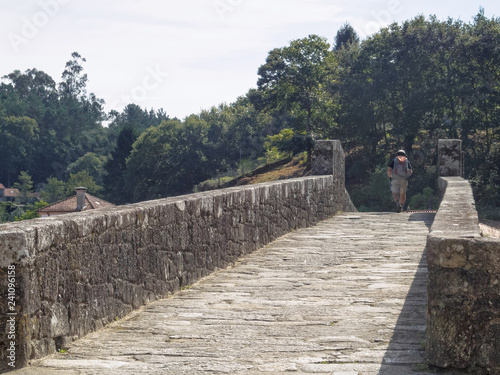 Pilgrim crosses the Tambre River on the old Maceira Bridge on the Camino Finisterre - Negreira, Galicia, Spain