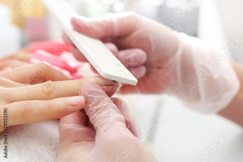 Usuwanie lakieru hybrydowego pilnikiem. Stylizacja paznokci, manicure w salonie kosmetycznym.