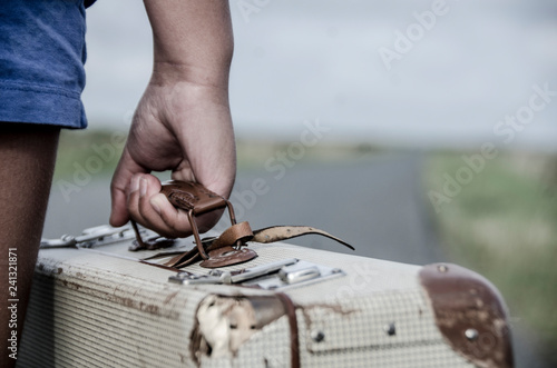 Refugee girl with a suitcase walking on the long road on the countryside