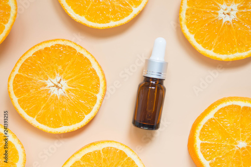 Natural vitamin c serum, skincare, essential oil products. Cosmetic brown glass vial w/ dropper and fresh juicy orange fruit slice on orange background. Beauty product branding mock-up. Top view.