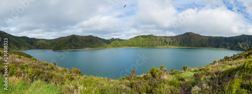 Panoramic landscape with beautiful blue crater lake Lagoa do Fogo from top of the hill on hiking trail. Lake of Fire is the highest lake of Sao Miguel island, surrounded by Natural Reserve green