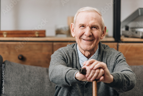 cheerful pensioner smiling and holding walking cane at home