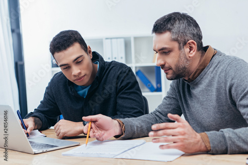 concentrated male coworkers working with papers and laptop in office