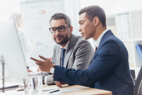 two professional businessmen discussing and using desktop computer in office