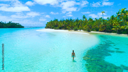 AERIAL: Woman walking in shallow ocean water surrounding One Foot Island.