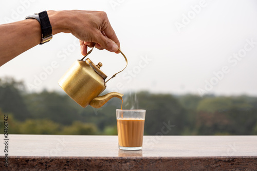 Hand pouring masala tea from a teapot into a glass.