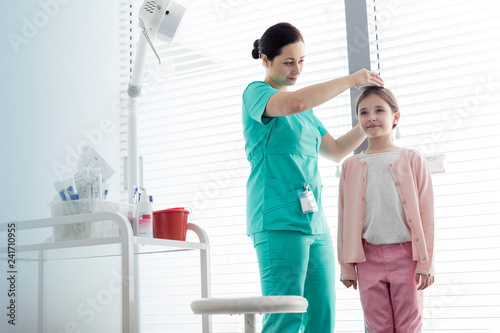 Nurse measuring height of girl against window at examination room