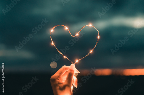 Simbolo del cuore fatto da una striscia di luci led tenuto da una mano di una ragazza di fronte al cielo sfuocato. San Valentino concetto.