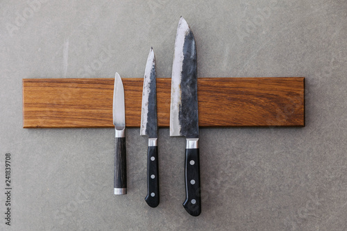 Dull Japanese kitchen knives stick on magnet cover with wood on concrete wall.