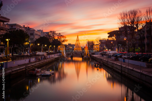 View of the Christmas Tree on a bridge at sunset, with orange clouds. Long exposure picture in Riccione, Emilia Romagna, Italy.