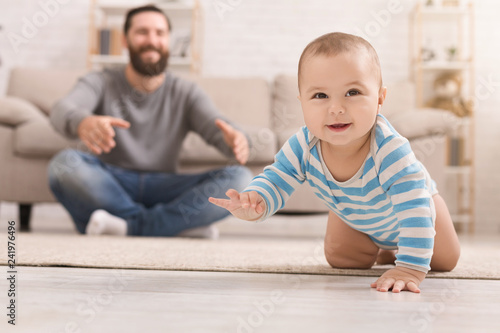 Adorable baby boy crawling on floor with dad