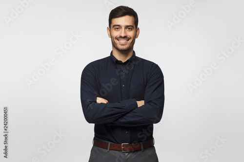 Modern businessman in deep blue shirt standing with crossed arms, isolated on gray background