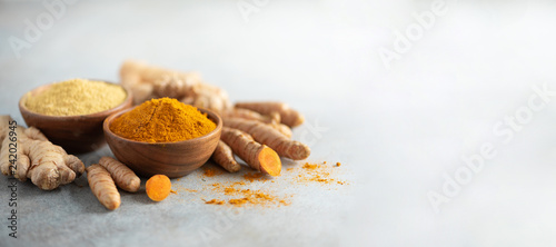 Turmeric and giger powder in wooden bowl and fresh turmeric root on grey concrete background. Banner with copy space
