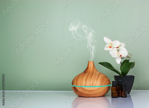 Electric Essential oils Aroma diffuser, oil bottles and flowers on light green surface with reflection