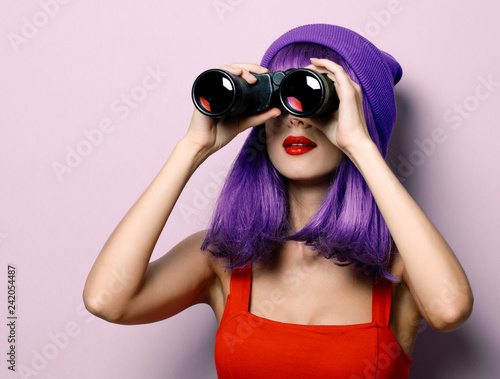 Portrait of young style hipster girl with blue hair and binoculars on purple color background