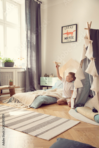 Little boy playing with toy airplane in scandinavian kid playroom with tent