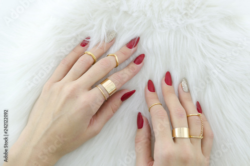 Woman hands with red nail art and jewelry on fur background.