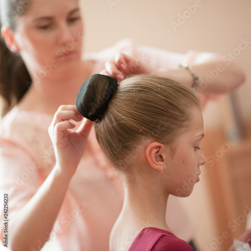 caring young mother woman fixing her little thin girl daughter hair bun