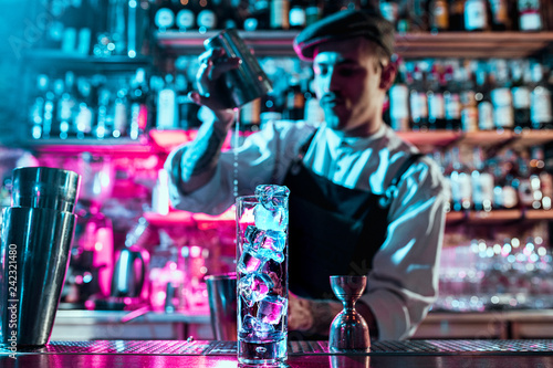 Expert barman is making cocktail at night club or bar. Glass of fiery cocktail on the bar counter against the background of bartenders hands with fire. Barman day concept