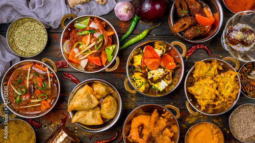 Assorted indian food set on wooden background. Dishes and appetisers of indeed cuisine, rice, lentils, paneer, samosa, spices, masala. Bowls and plates with indian food