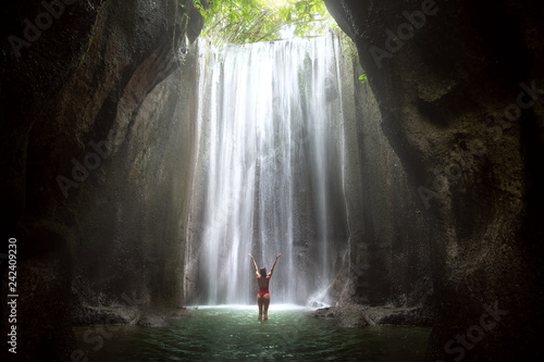 Woman with arms raised to gorgeous scenic epic majestic waterfall in cave with light rays