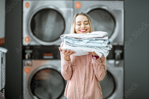 Young woman enjoying clean ironed clothes in the self serviced laundry with dryer machines on the background