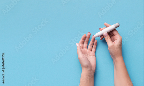 Woman using glucometer on blue background, top view