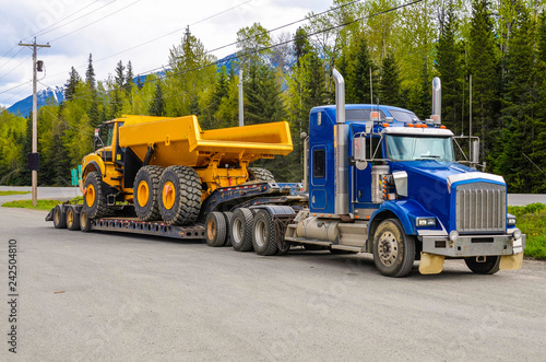 Big truck with a low platform trailer carrying a tipper truck on a public parking area of a truck stop