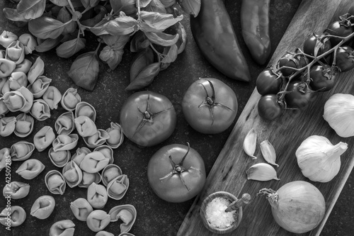 Italian food ingredients. Tortellini pasta, herbs and vegetables. Black and white photo.