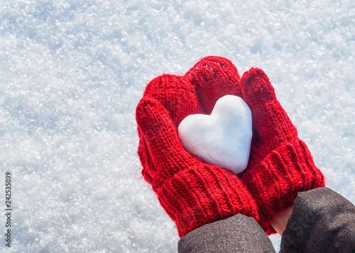 Female hands in knitted mittens with heart of snow in winter day. Love concept. Valentine day background.