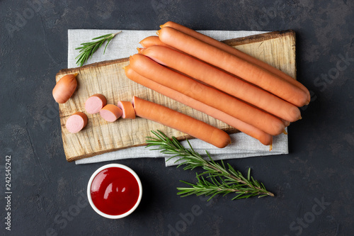 Raw frankfurter sausages with ketchup on cutting board. Top view.