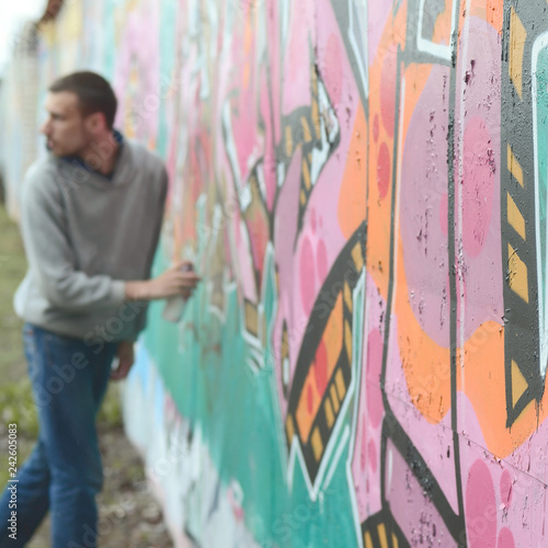 A young guy in a gray hoodie paints graffiti in pink and green c