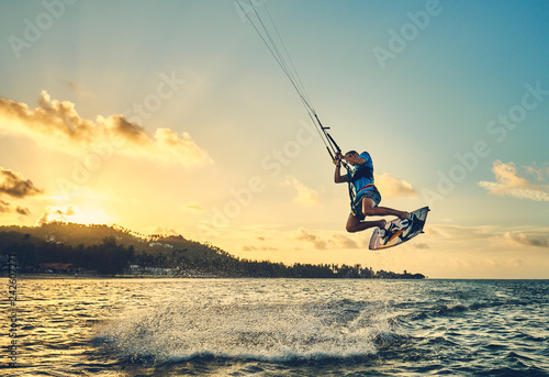 Young man kite boarder jumps over the sea at sunset 